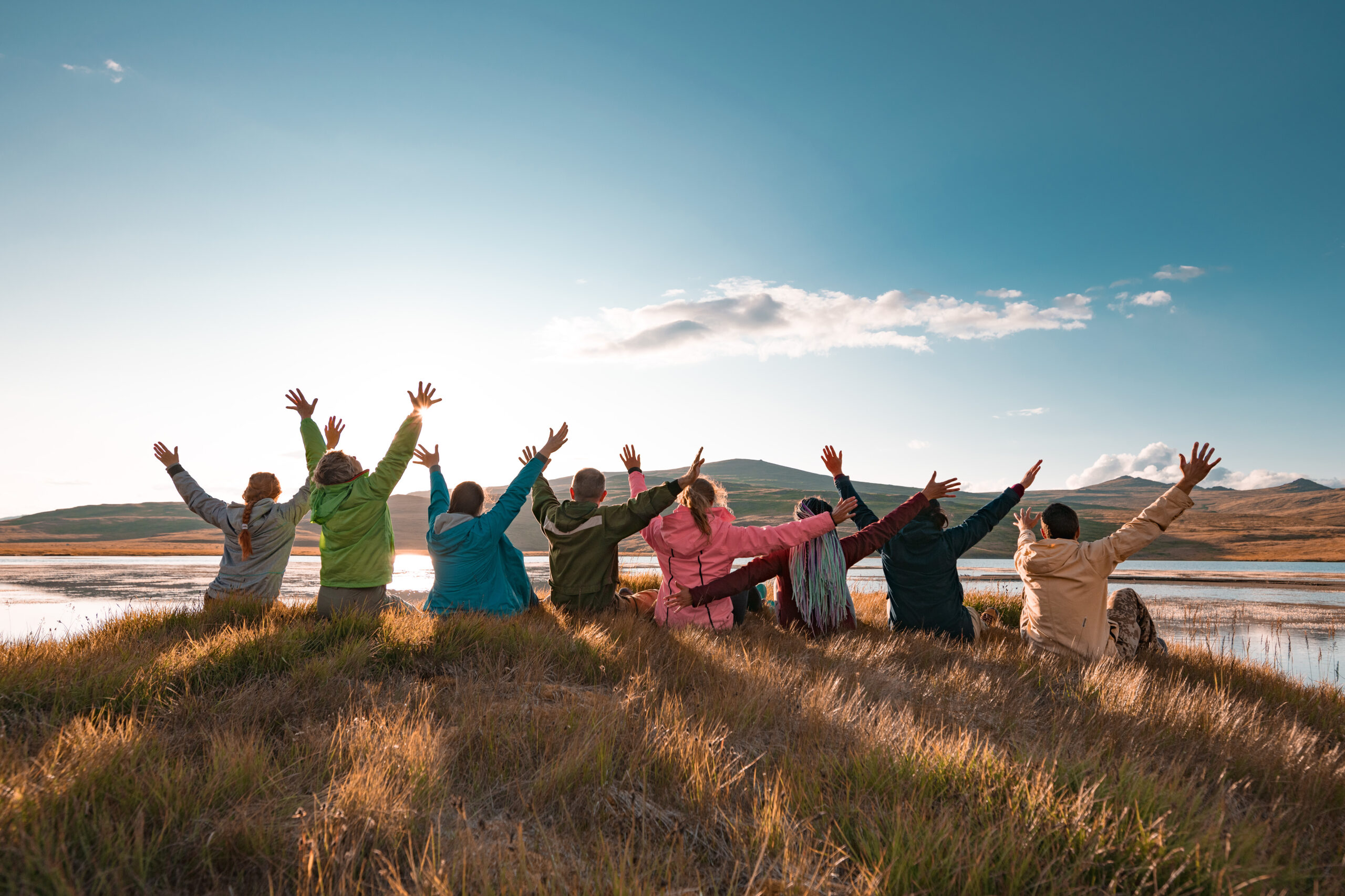 Group of people sitting with raised arm beautiful sunset lake and mountains